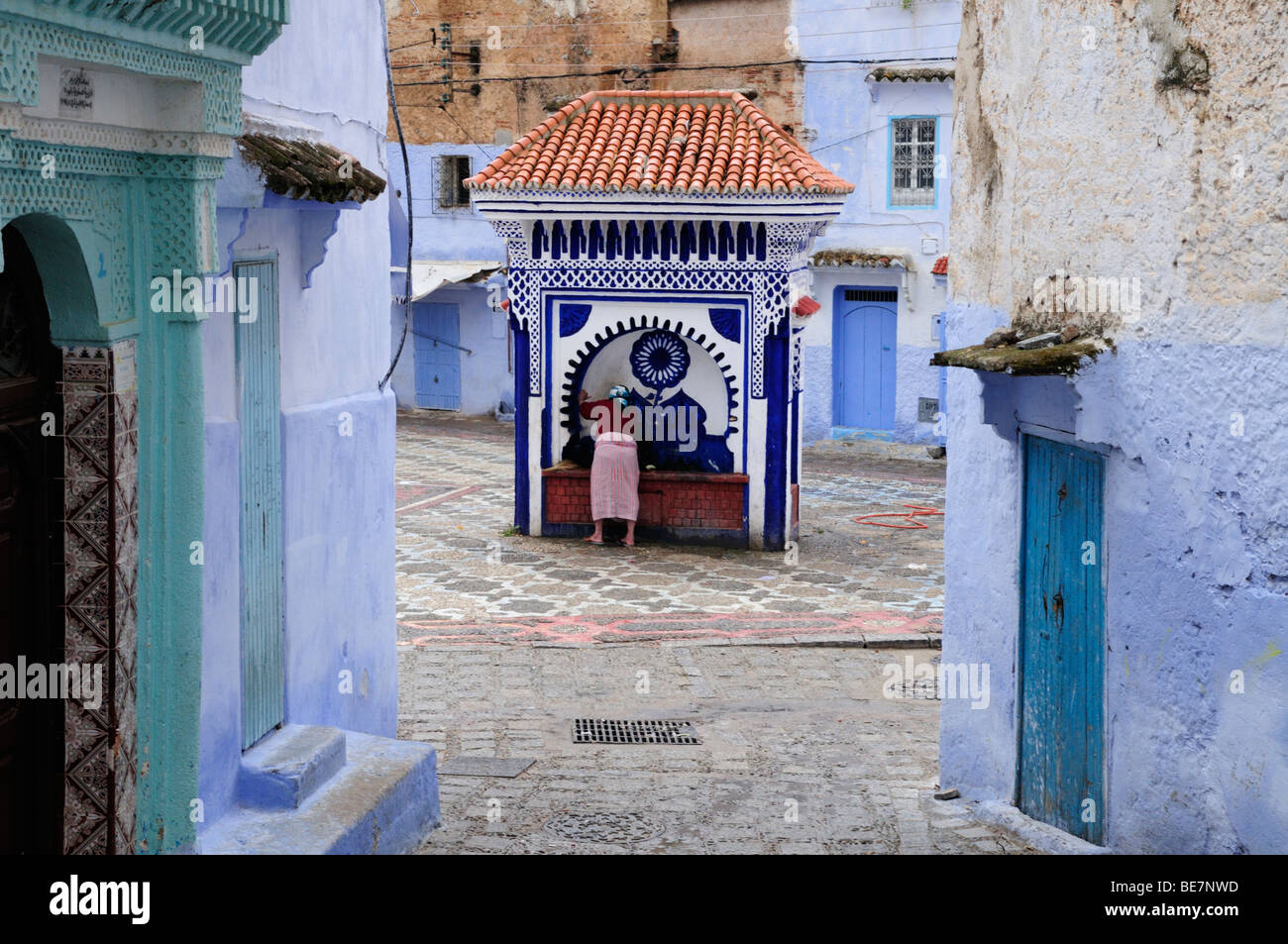 Il Marocco; Chefchaouen; Scene di strada nella Medina che mostra una donna ad una delle pubbliche fontane di acqua Foto Stock