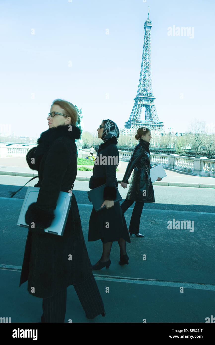 Tre donne a piedi, tutti vestiti in bianco e nero e trasportano i computer laptop, Torre Eiffel in background Foto Stock