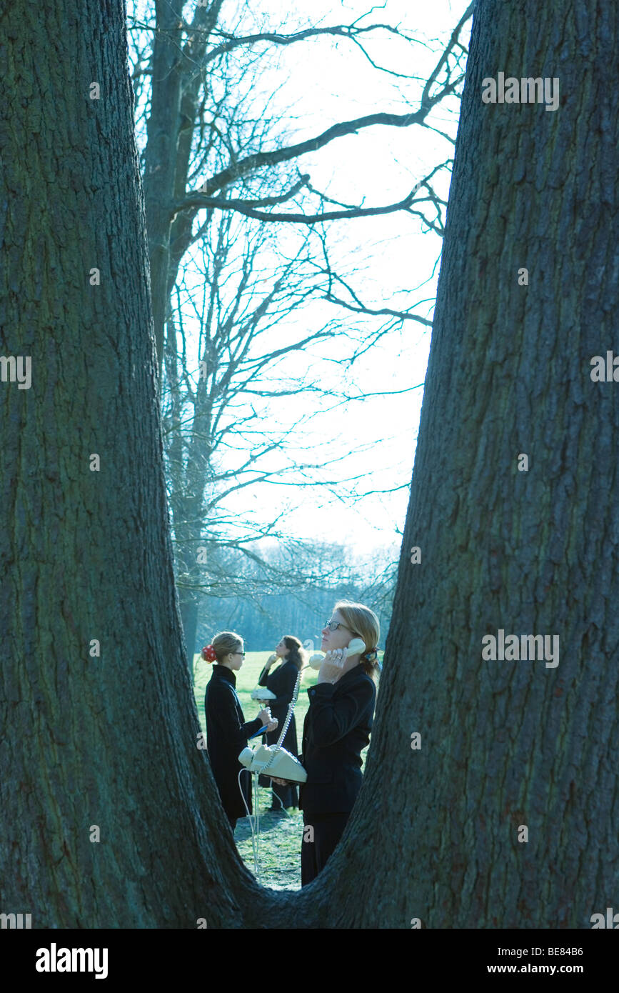 Le femmine in piedi all'aperto, utilizzando i telefoni di rete fissa, visto attraverso tronchi di alberi Foto Stock