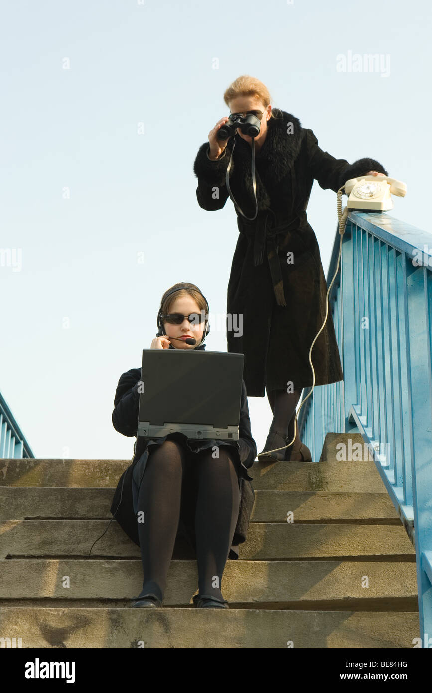 Due femmine su gradini vestite di nero utilizzando laptop, binocolo Foto Stock