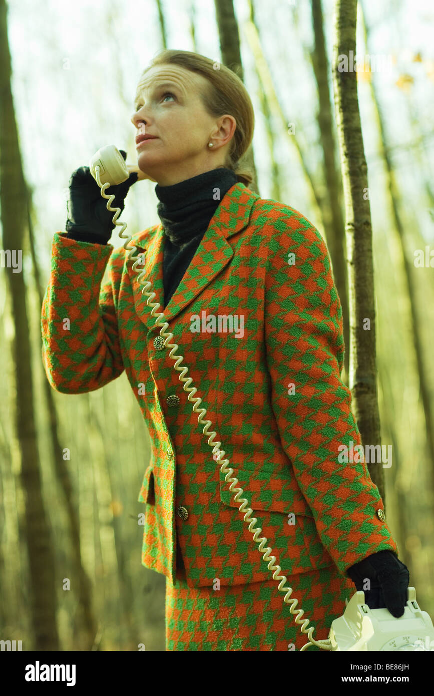 Donna in piedi nei boschi, utilizzando il telefono di rete fissa, guardando verso l'alto Foto Stock