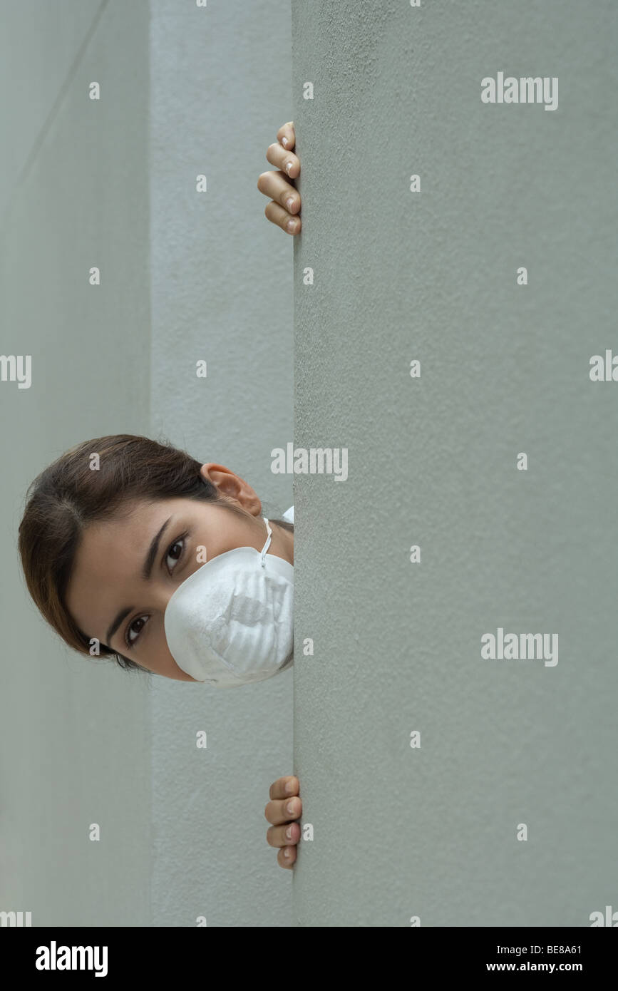 La donna nella maschera di inquinamento spiata dietro l'angolo Foto Stock