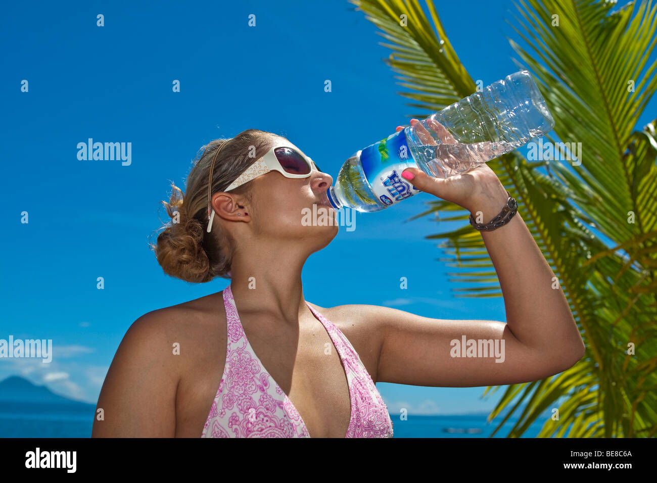 Giovane donna sulla spiaggia a bere da una bottiglia di acqua, Indonesia, sud-est asiatico Foto Stock