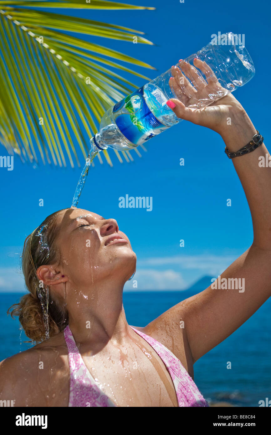 Giovane donna sulla spiaggia versando acqua da una bottiglia di acqua sopra la testa, Indonesia, sud-est asiatico Foto Stock