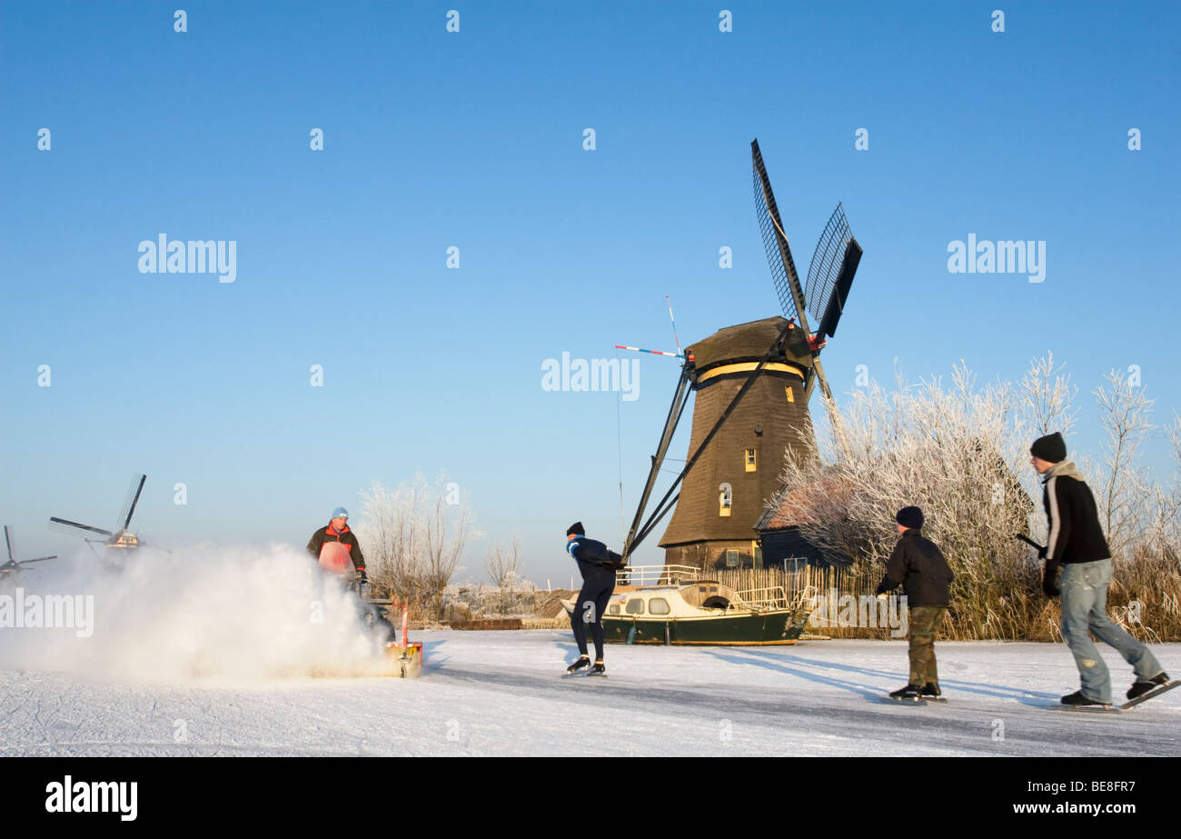 Pattinaggio sul ghiaccio pattino lungo i mulini a vento di Kinderdijk mentre il ghiaccio viene pulito Foto Stock