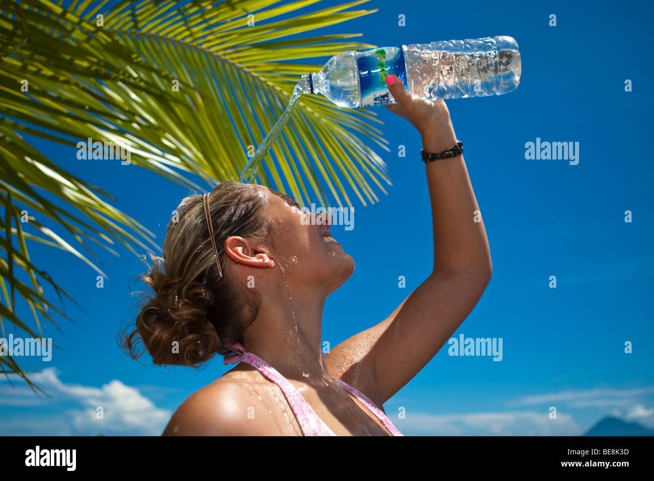 Giovane donna sulla spiaggia versando acqua da una bottiglia di acqua sopra la testa, Indonesia, sud-est asiatico Foto Stock