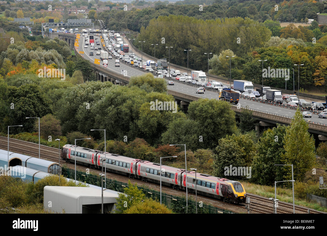 Un treno dei pendolari in esecuzione accanto al traffico di accodamento su elevati autostrada M6 in direzione nord vicino al Birmingham ,REGNO UNITO Foto Stock