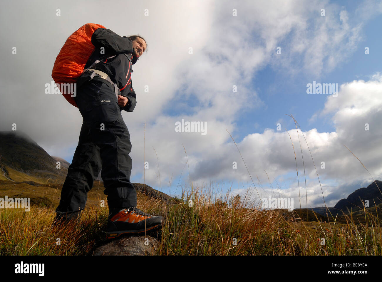 Escursionista con zaino sulla strada nelle montagne scozzesi in moody nuvole nel cielo, Highlands scozzesi, Liathach, Torridon, S Foto Stock