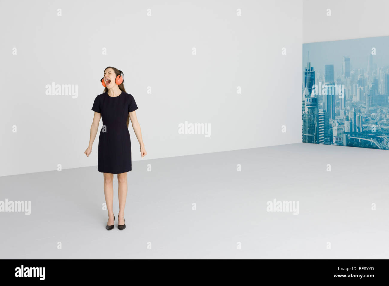 Donna che indossa le cuffie di protezione, gridando, cityscape in background Foto Stock