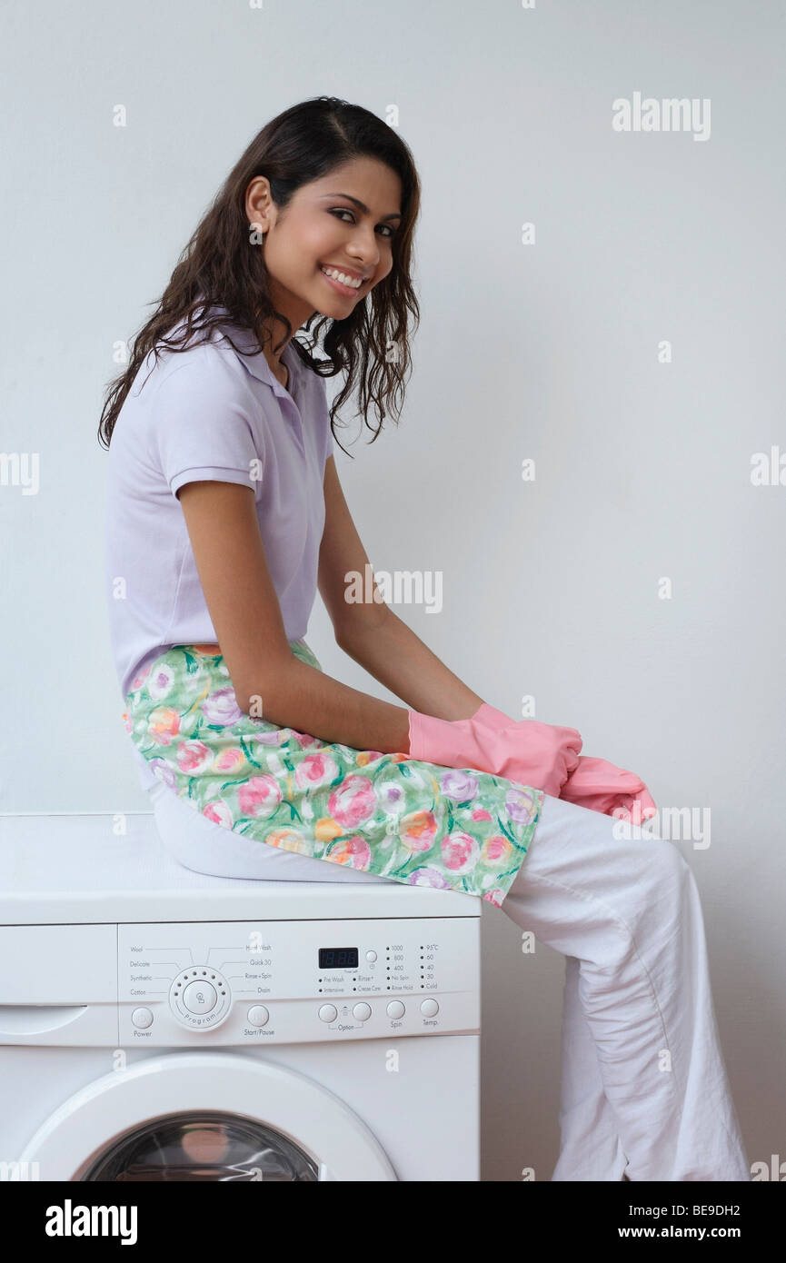Donna con guanti seduto sulla macchina di lavaggio e sorridente in telecamera Foto Stock