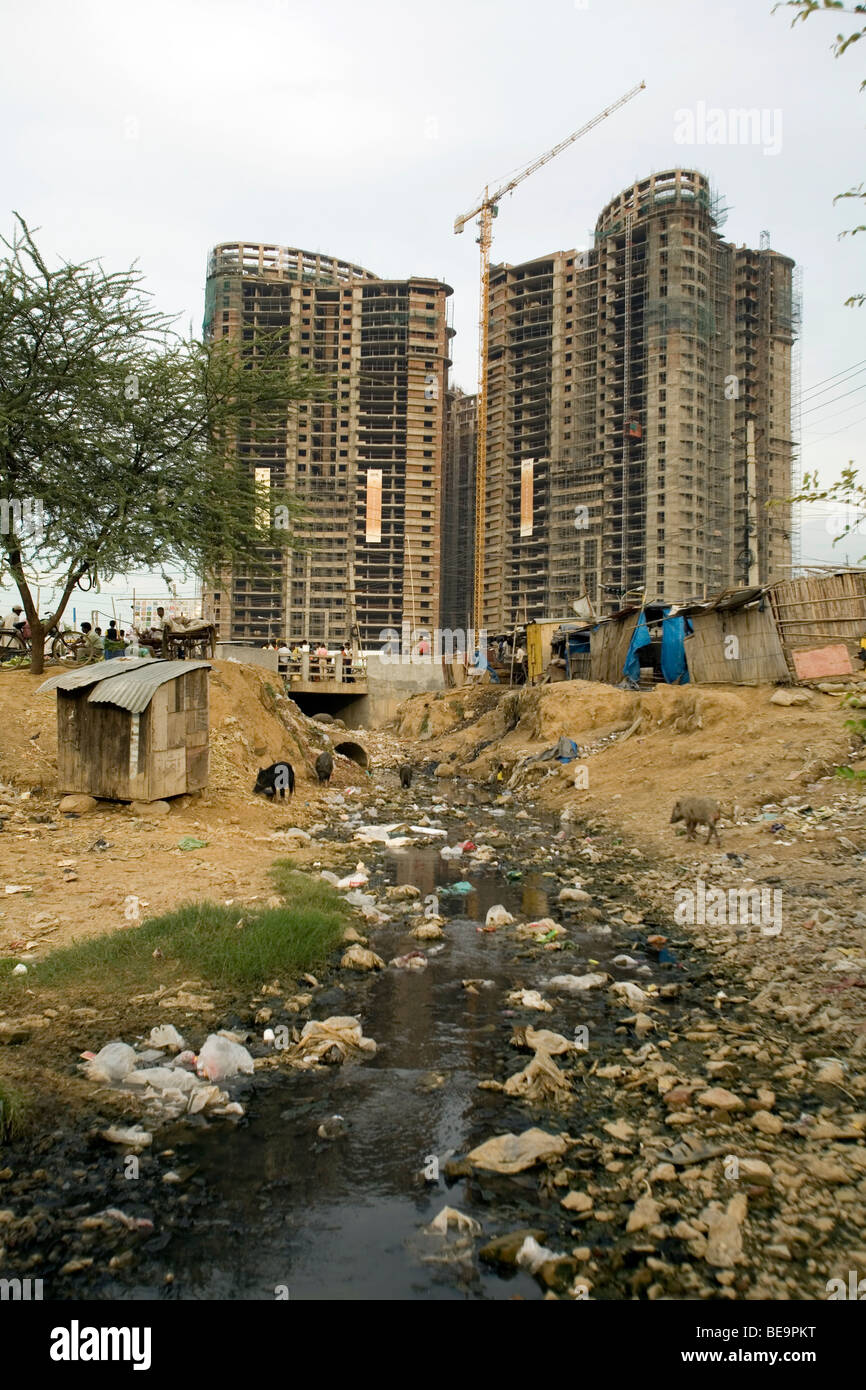 Costruire baracche di lavoratori, un tombino aperto e suini di fronte ad una nuova costruzione in Gurgaon, India Foto Stock