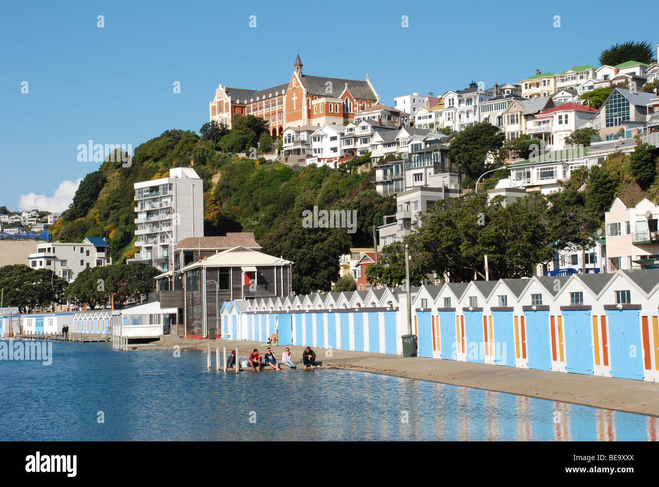 Spiaggia di capanne / rifugi di vela sul lungomare di Wellington, Oriental Parade, Nuova Zelanda, con monastero in background. Foto Stock