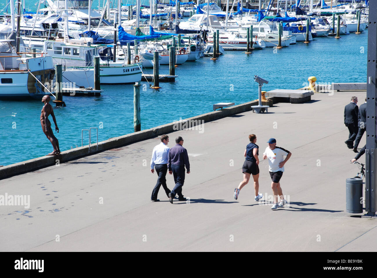 Per gli amanti del jogging tenersi in forma, mentre gli uomini d' affari passeggiare al sole, il lato del porto; con barche e statua di Wellington, Nuova Zelanda. Foto Stock