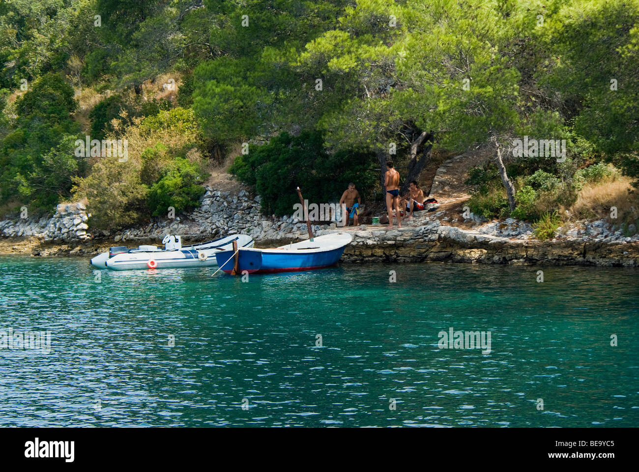 Croazia; Hrvartska; Kroatien, Isola di Hvar bay; 3 giovani uomini riposo dopo la nuotata nella bellissima isola croata bay, 2 piccole imbarcazioni Foto Stock