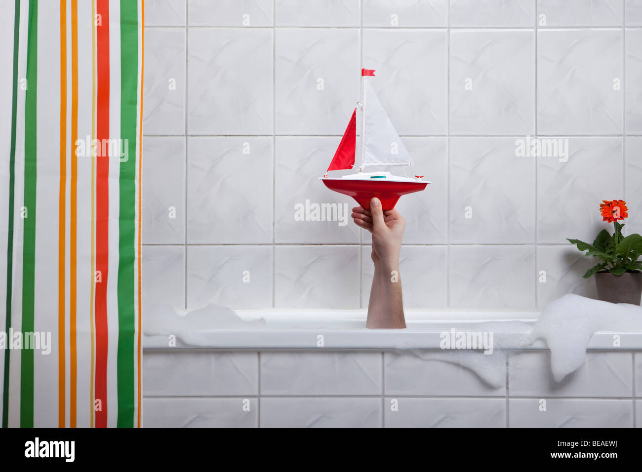 Una mano umana fuori di una vasca da bagno in possesso di una barca giocattolo Foto Stock