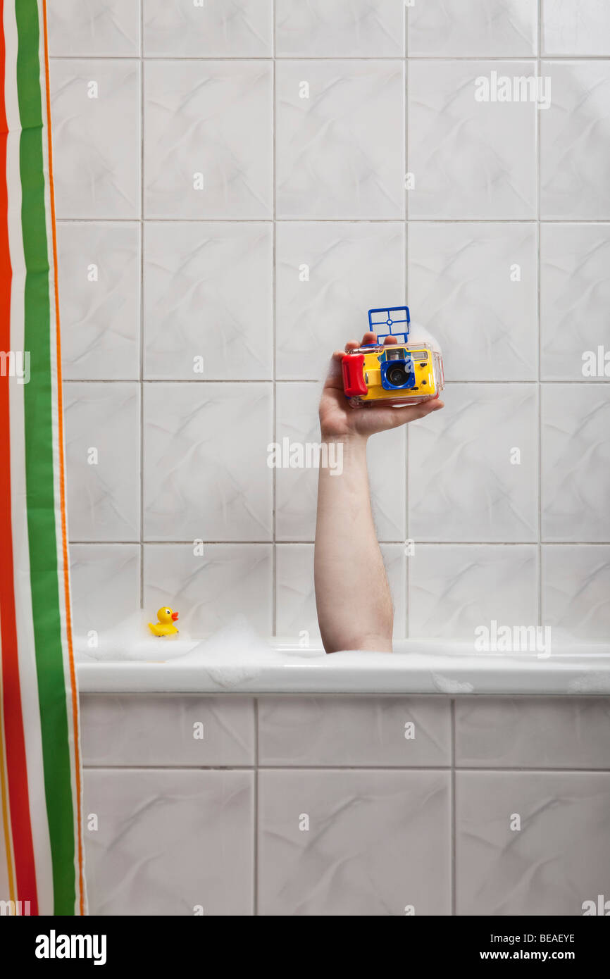 Una mano umana fuori di una vasca da bagno tenendo una fotocamera subacquea Foto Stock