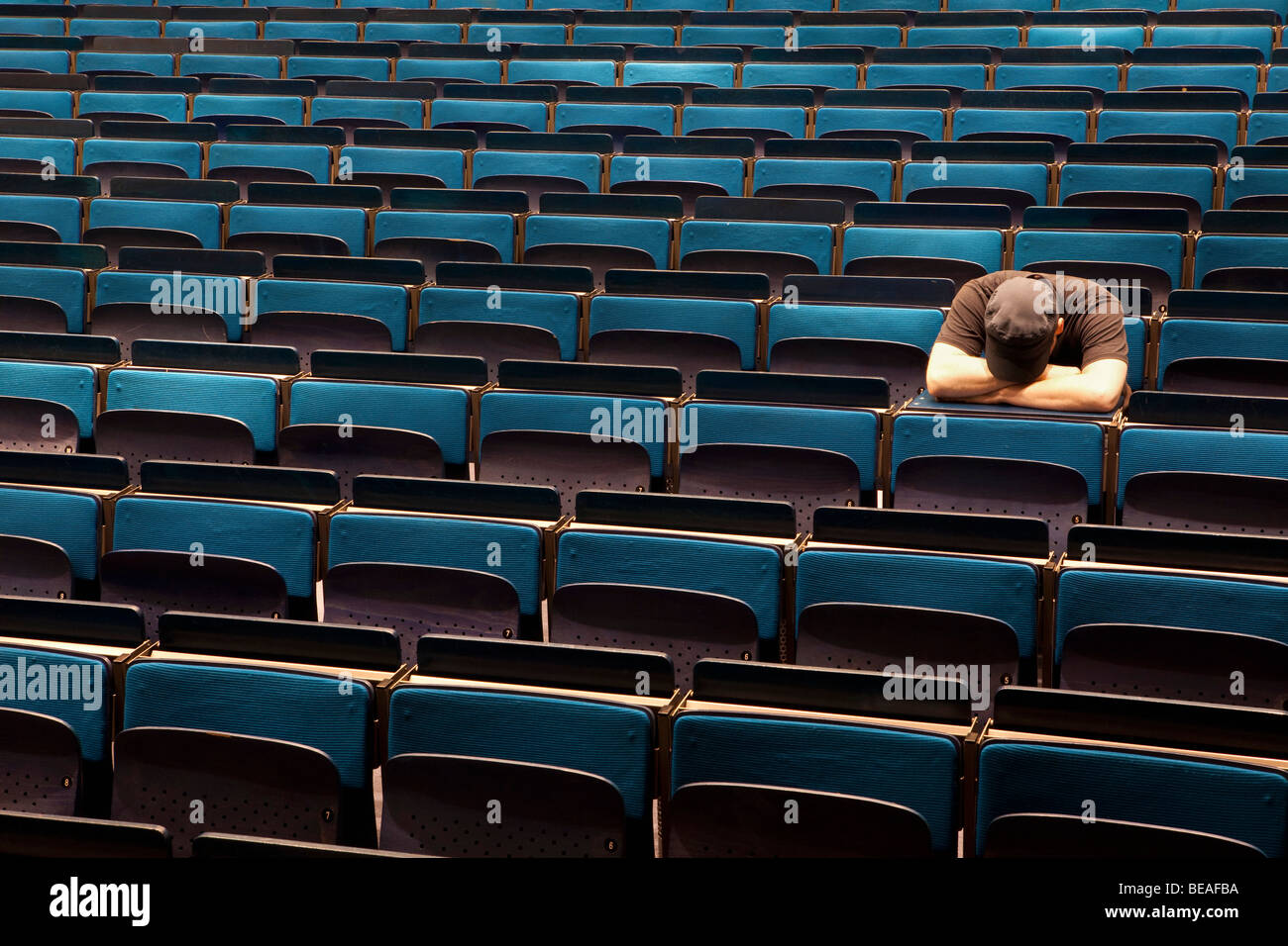 Un uomo seduto in un auditorium con la sua testa in appoggio nelle sue braccia Foto Stock
