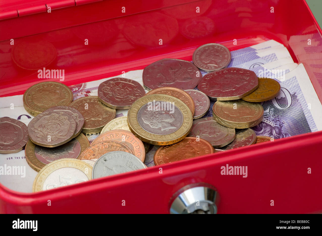Un metallo rosso bloccabile Petty Cassa contenente British denaro con le monete nel fuoco Foto Stock