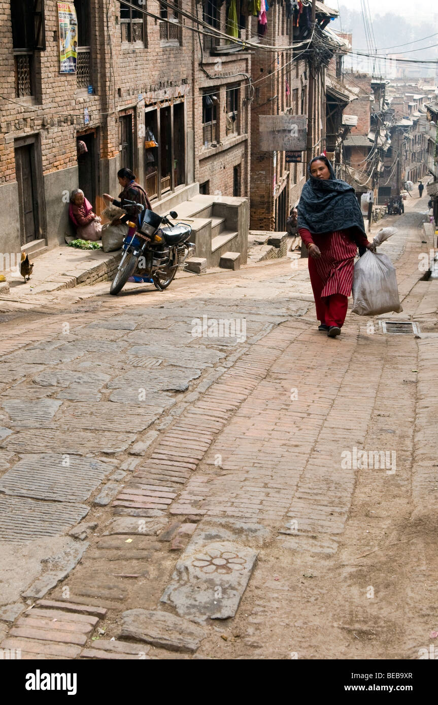 Donna locale borsa da trasporto in salita verso la piazza della città vecchia, Bhaktapur, Nepal Foto Stock