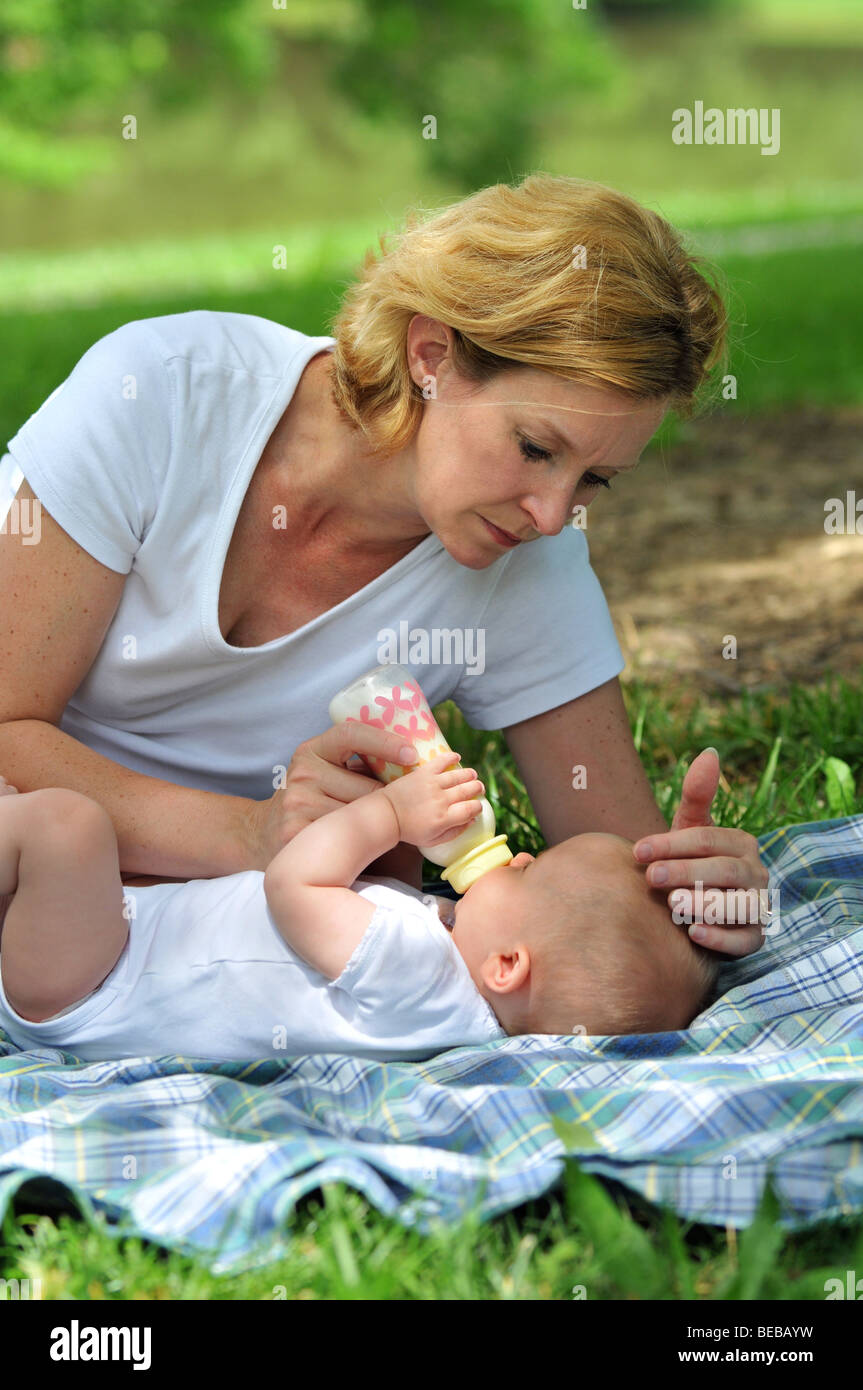 Madre aiutare il bambino bere latte dal flacone all'aperto Foto Stock