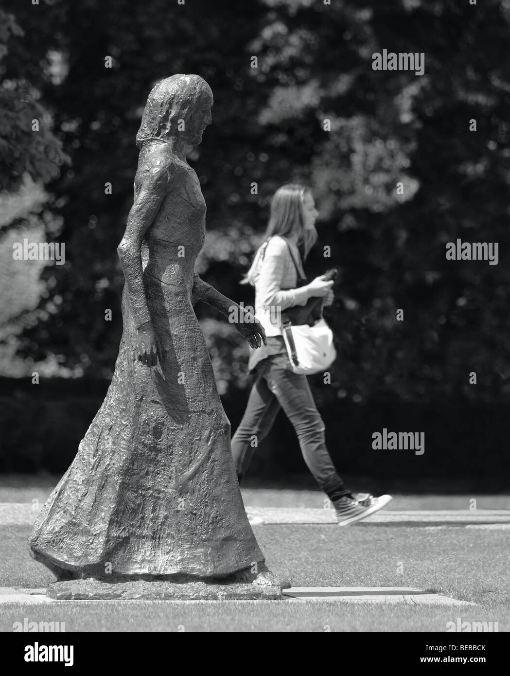 Una ragazza camminare passato una scultura da Elizabeth Frink riecheggia la posa della scultura. Foto Stock