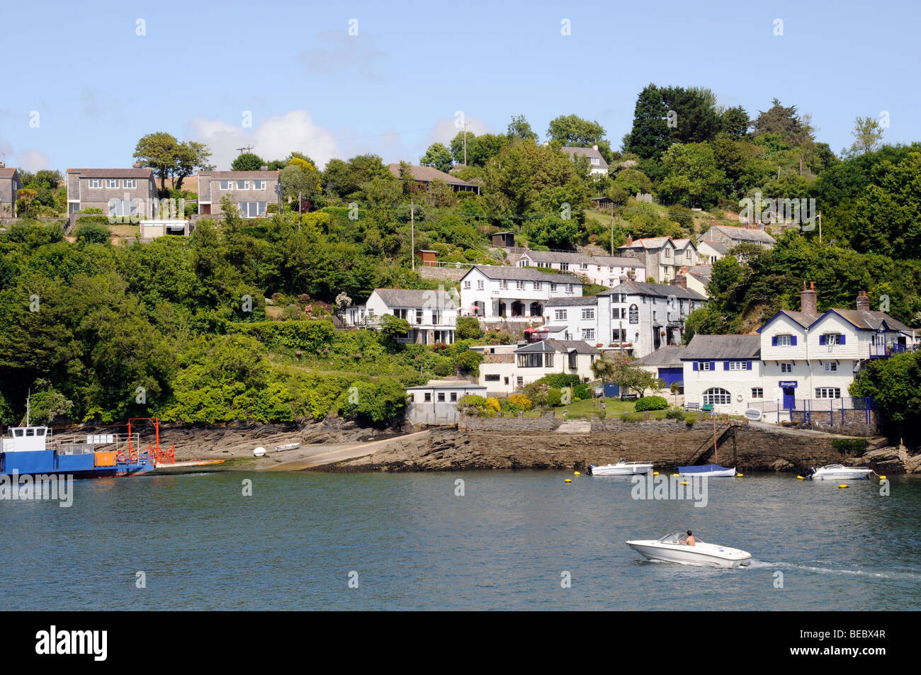 Una piccola imbarcazione a motore si avvicina le vetture che viaggiano attraverso il Fowey estuario sull'Fowey traghetto per auto su un cielo blu, giornata di sole. Foto Stock