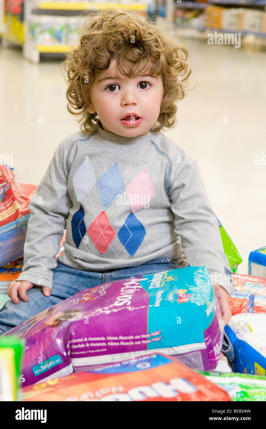 Bambino seduto con pacchetti di pannolino intorno a lui in un supermercato Foto Stock