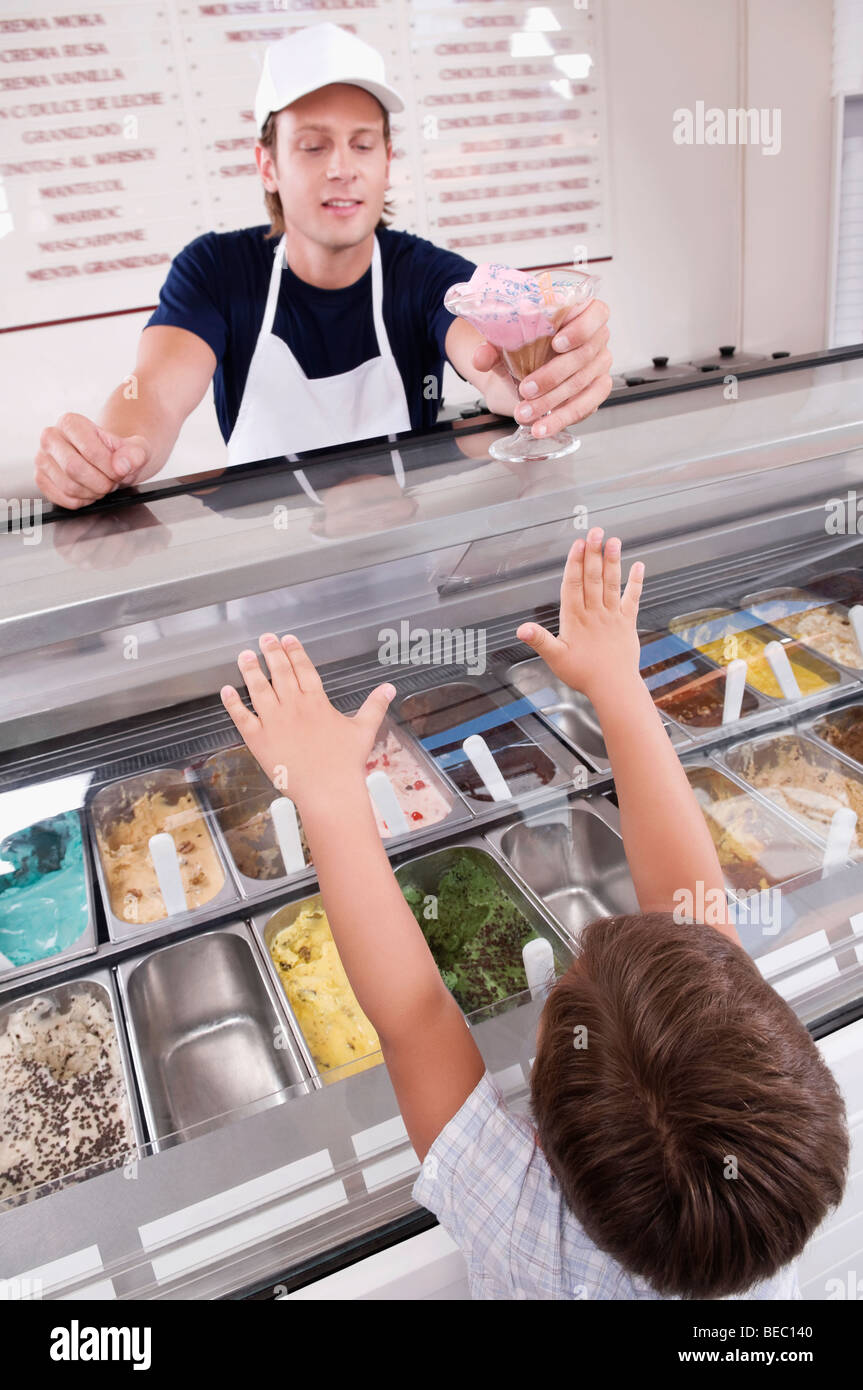 Addetto alle vendite dando il gelato ad un ragazzo in una gelateria Foto Stock