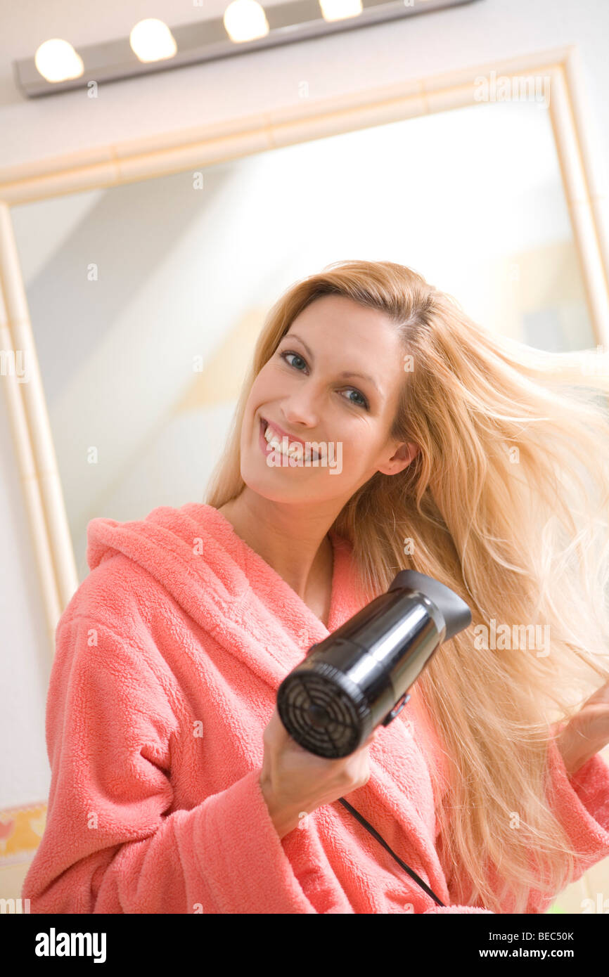 Giovane donna l'asciugatura dei capelli con asciugacapelli in bagno. Foto Stock