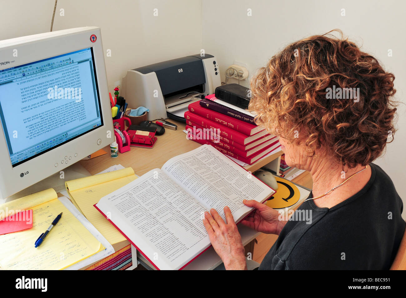 Copy-Editor femmina lavorando davanti a un computer la modifica di un documento accademico con l aiuto di un dizionario e altri libri di testo Foto Stock
