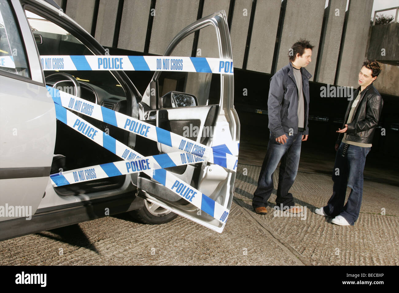 Auto con lo sportello aperto e nastro di polizia e due giovani uomini Foto Stock