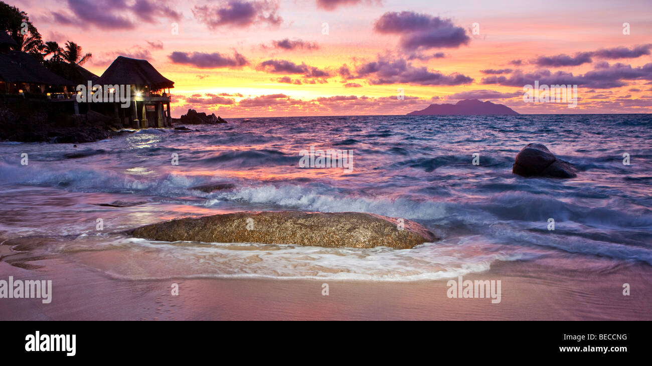 Tipico di roccia di granito delle Seicelle sulla spiaggia al tramonto vicino Glacis, Sunset Beach Resort sul retro, Isola di Mahe, Seychelle Foto Stock