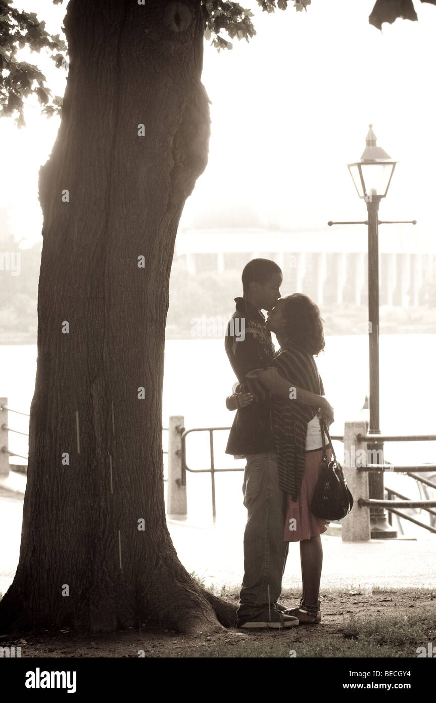 Stagliano giovane rifugio dalla pioggia sotto un albero mentre si tiene ogni altro in un romantico abbraccio. Foto Stock