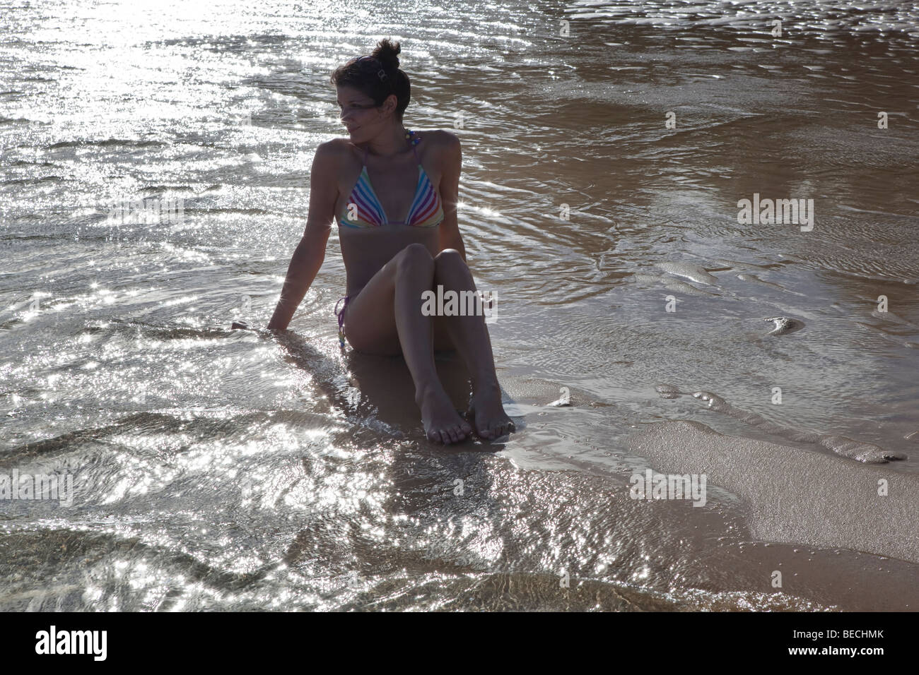 Giovane donna seduta su una spiaggia deserta a Rarotonga nelle Isole Cook nel Pacifico del Sud Foto Stock