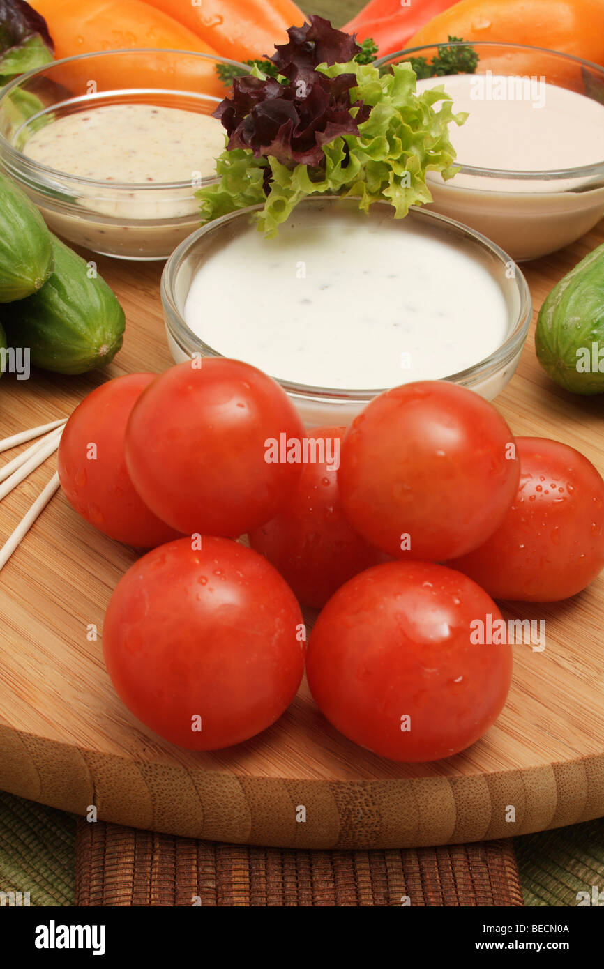 Miniatura capsicum, cocktail pomodori, cetriolino in miniatura, lattuga, salsa di yogurt, American dip, senape-miele dip su un taglio di legno Foto Stock
