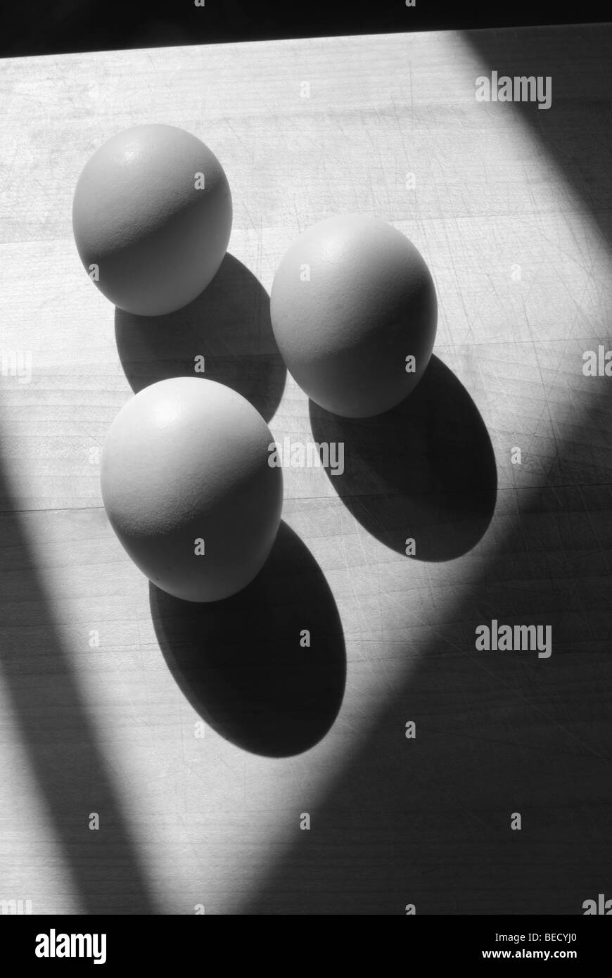 Tre uova su un tagliere di legno,ombre profonde e in bianco e nero, monocromatiche, nessuno.ancora in vita. Foto Stock