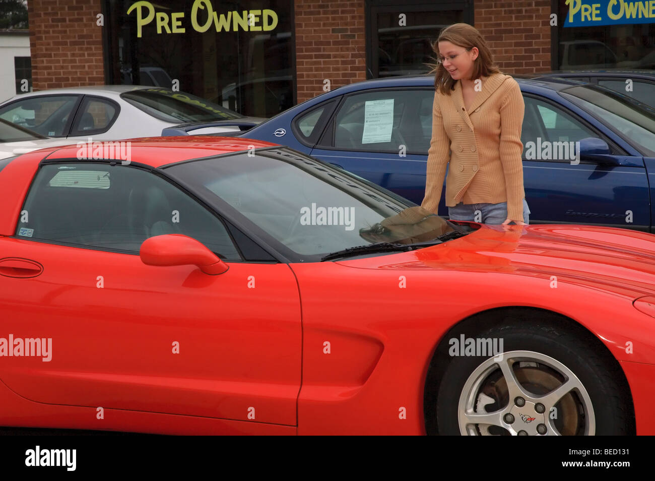 Una ragazza adolescente guardando il suo sogno auto, un rosso corvette, in una automobile usata molto. Foto Stock