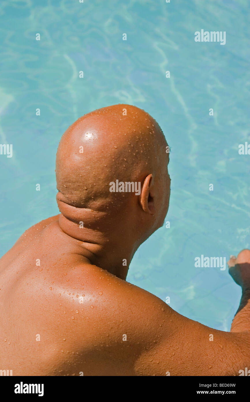 Bald senior citizen seduta sul bordo di una piscina Foto Stock