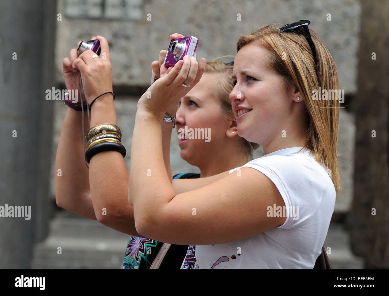 Due giovani donne bionda ragazze scattare una fotografia del Duomo di Milano dalla giunzione di Piazza del Duomo e Corso Vittorio Emanuele Foto Stock