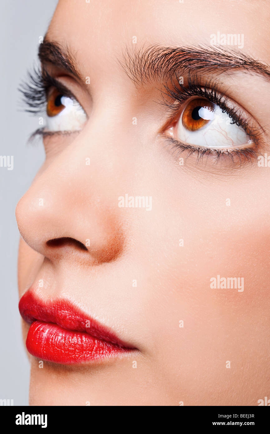Close up volto ritratto di una donna con grandi occhi marroni e rosso brillante labbra Foto Stock