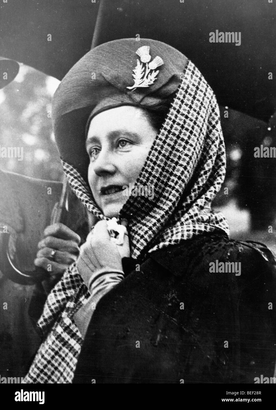 Elizabeth Bowes-Lyon, la regina consorte, mette una sciarpa sopra il suo cappello contro la pioggia. Foto Stock