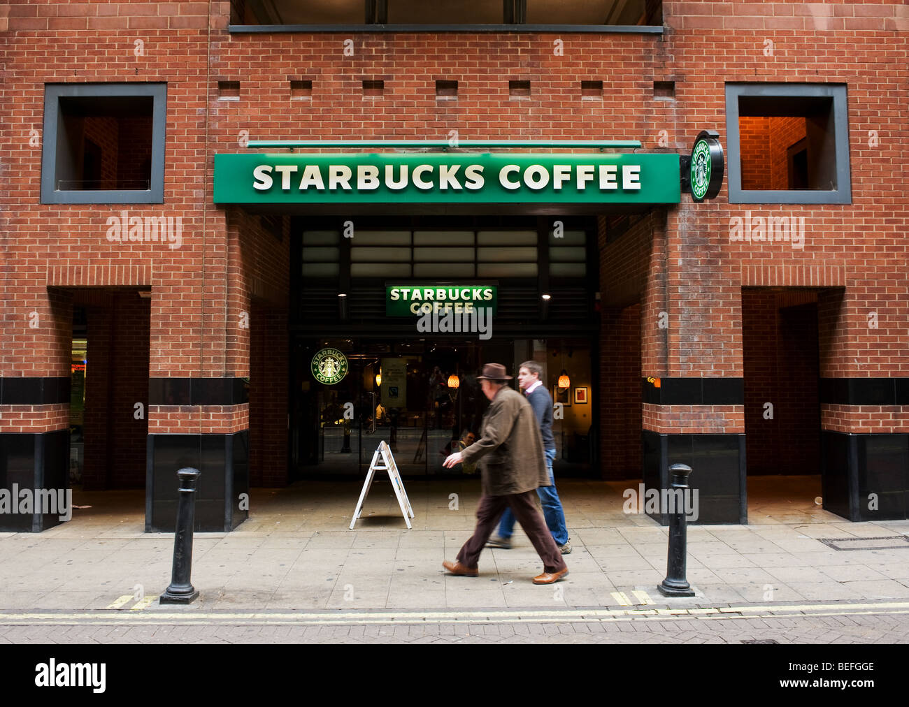 Due maschi camminare davanti a un caffè Starbucks a Londra. Foto Stock