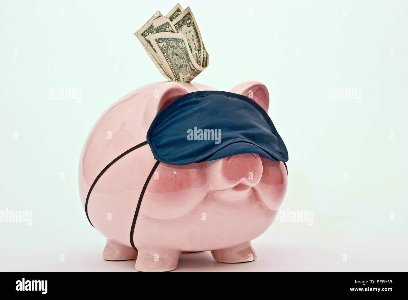 Salvadanaio con le fatture del dollaro nella slot di moneta che indossa una maschera di sospensione Foto Stock