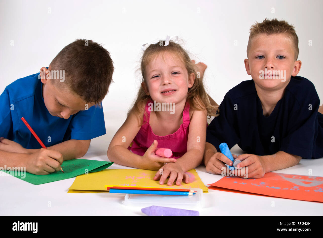 Tre bambini sdraiato sul pavimento colorazione brillante su carta colorata. Foto Stock