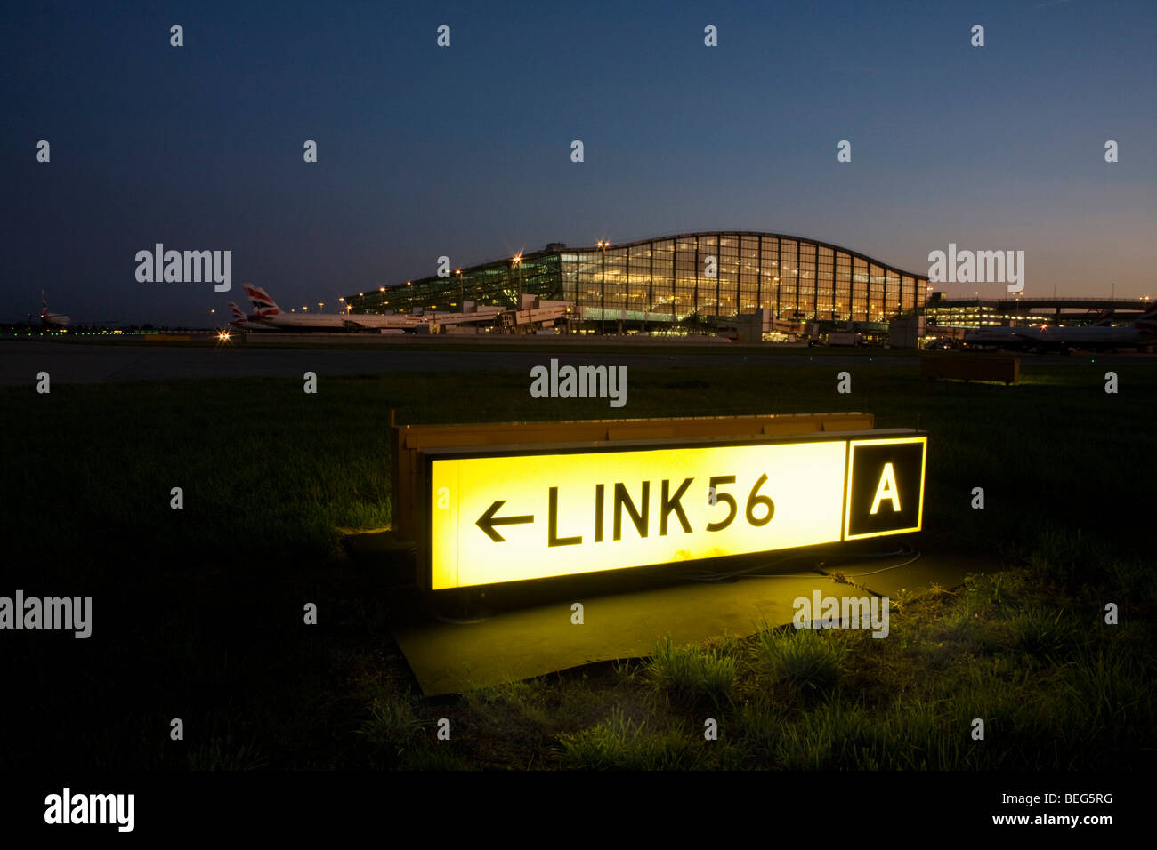 Un esterno crepuscolo di visualizzazione del terminale 5 e la costruzione di una pista di rullaggio segno per i piloti per navigare complicato l'aeroporto di Heathrow Foto Stock