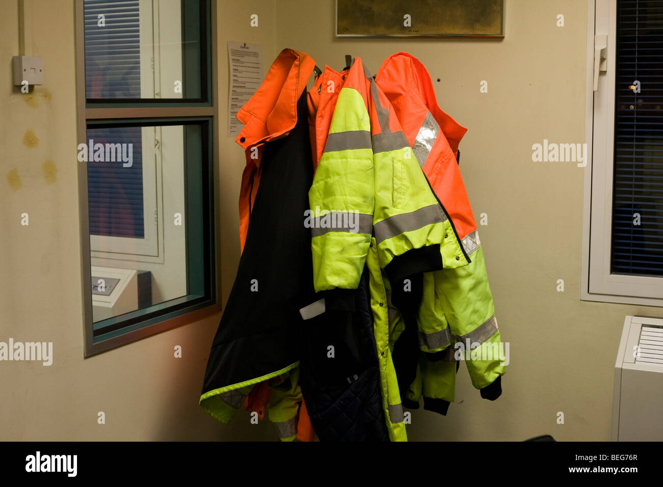 Alta visibilità giacche appendere su un appendiabiti appartenenti ad operazioni Airside unità di sicurezza (AOSU) personale presso l'aeroporto di Heathrow. Foto Stock