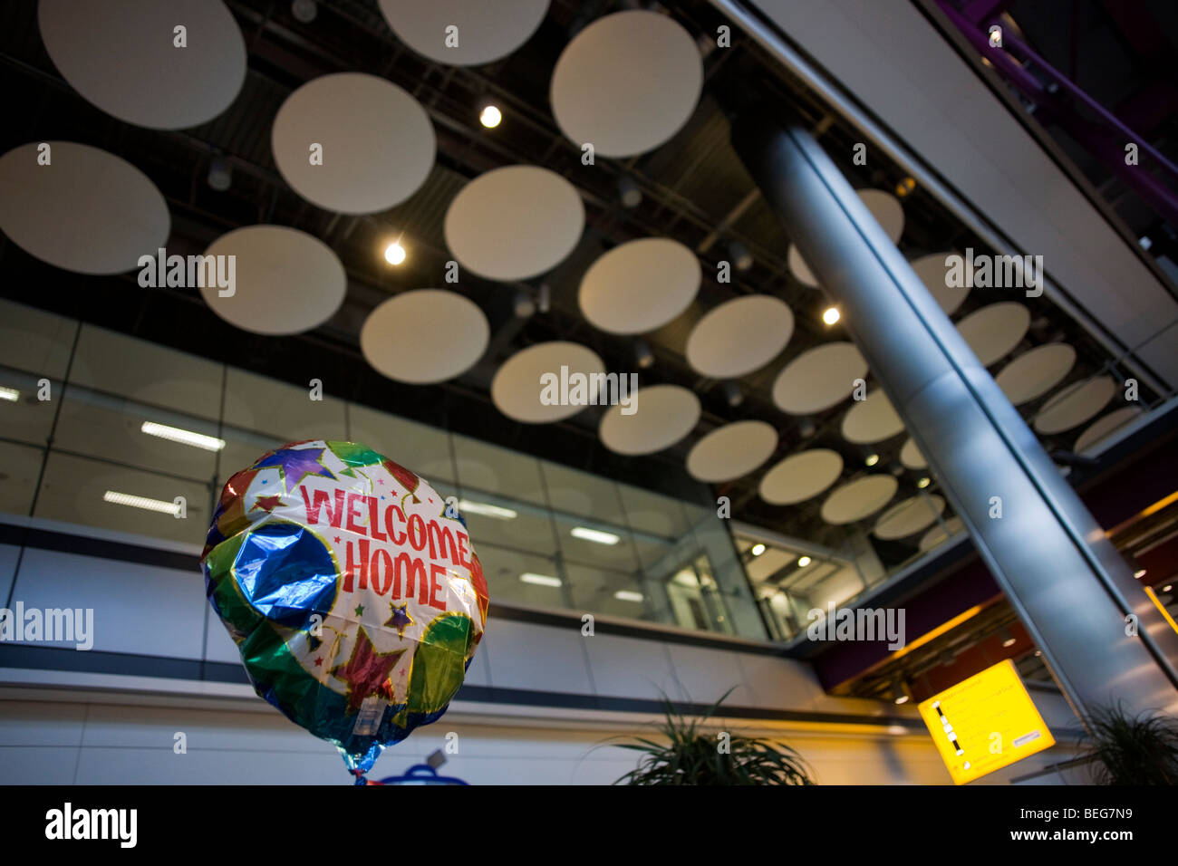 Un elio-riempito Benvenuti Home palloncino di una famiglia in attesa di cari galleggianti in aria in aeroporto di Heathrow T5 Foto Stock