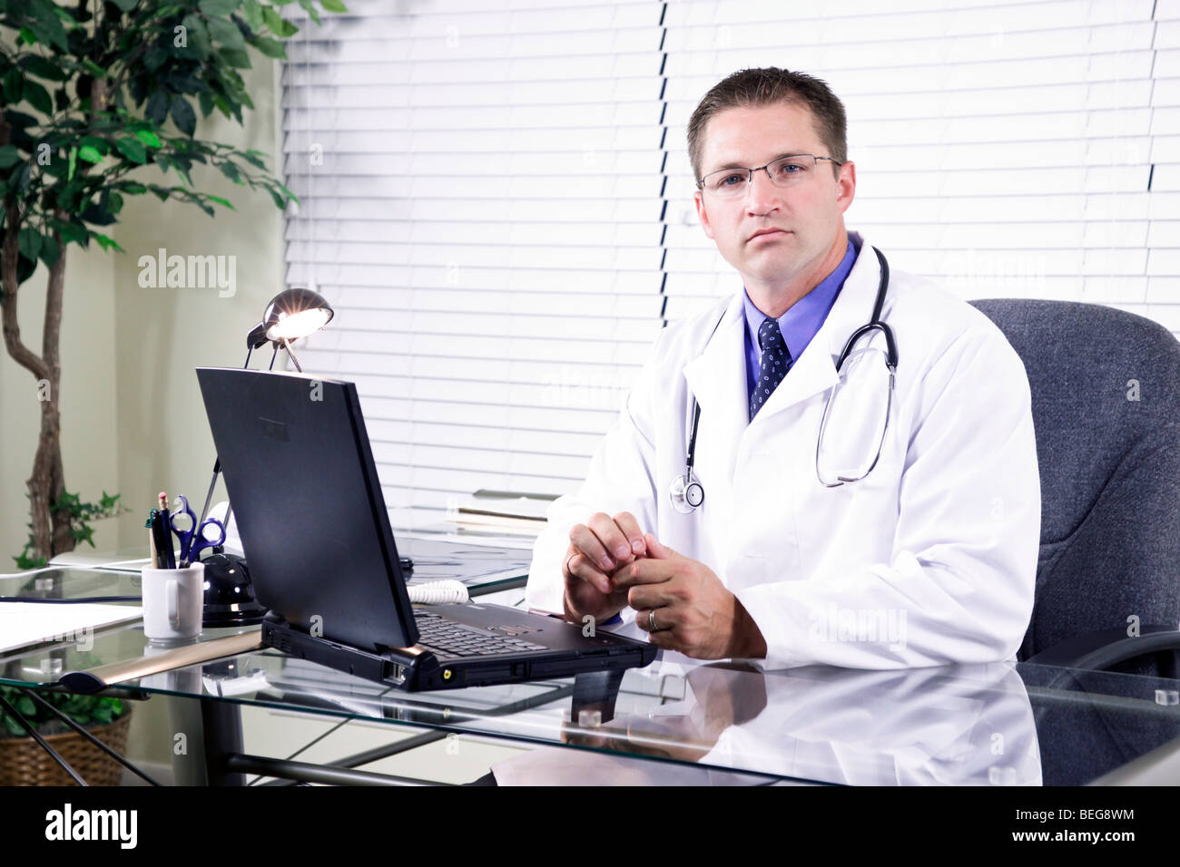 Una solenne giovane medico seduto nel suo ufficio, guardando c'erano pochi sorrisi alla telecamera. Foto Stock