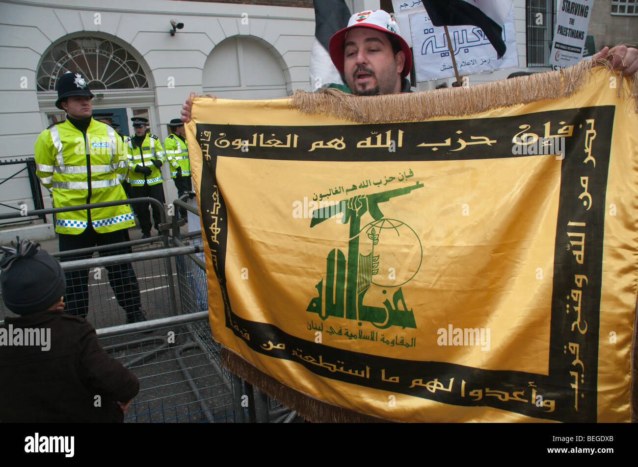 La polizia al di fuori dell'ambasciata egiziana e uomo con la bandiera di Hezbollah a protestare chiamando per frontiera Gaza per essere riaperta Foto Stock
