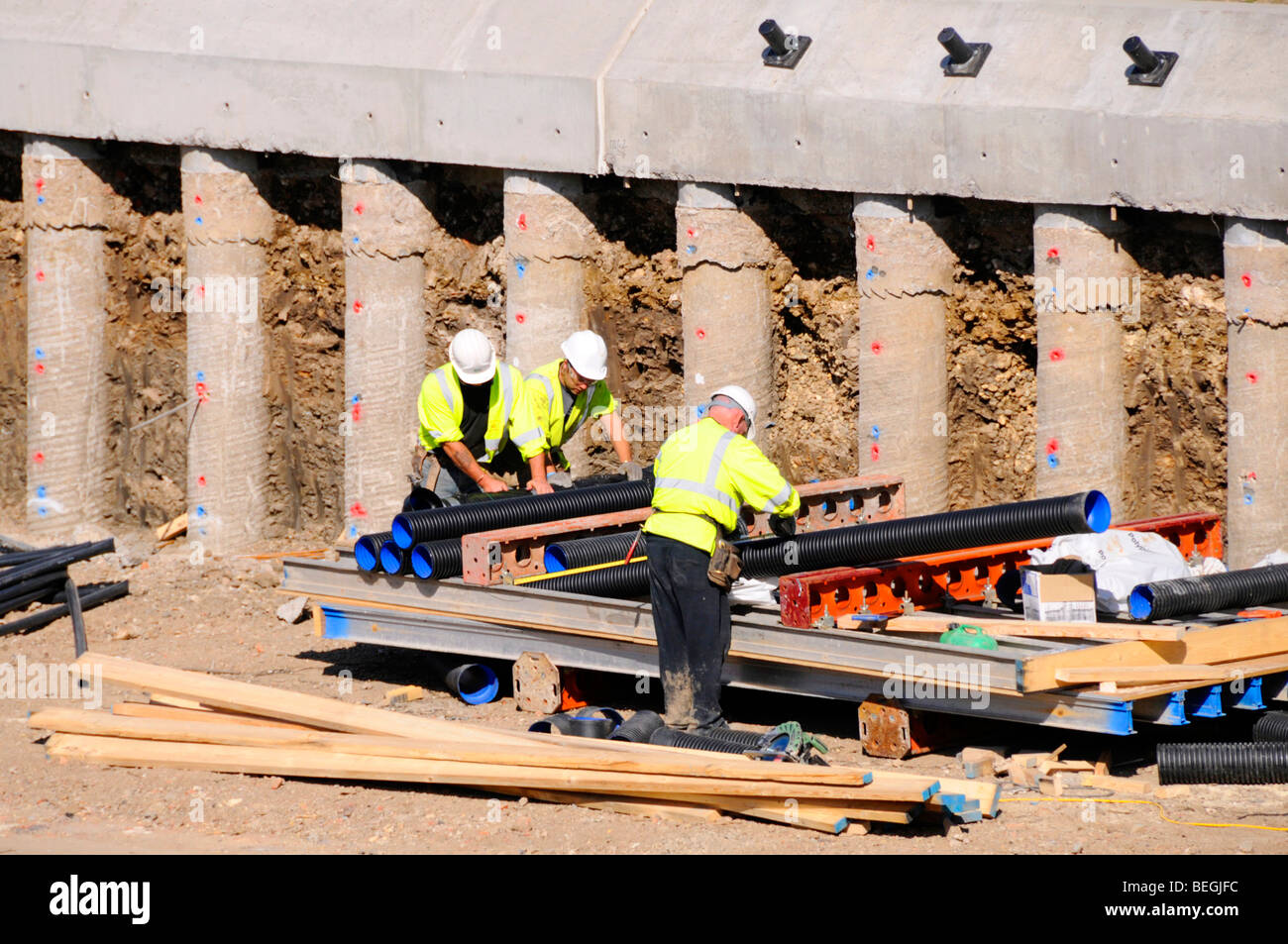 Operai accanto esposti pali in calcestruzzo che forma parte di una parete di ritegno per la struttura di un ponte autostradale Foto Stock